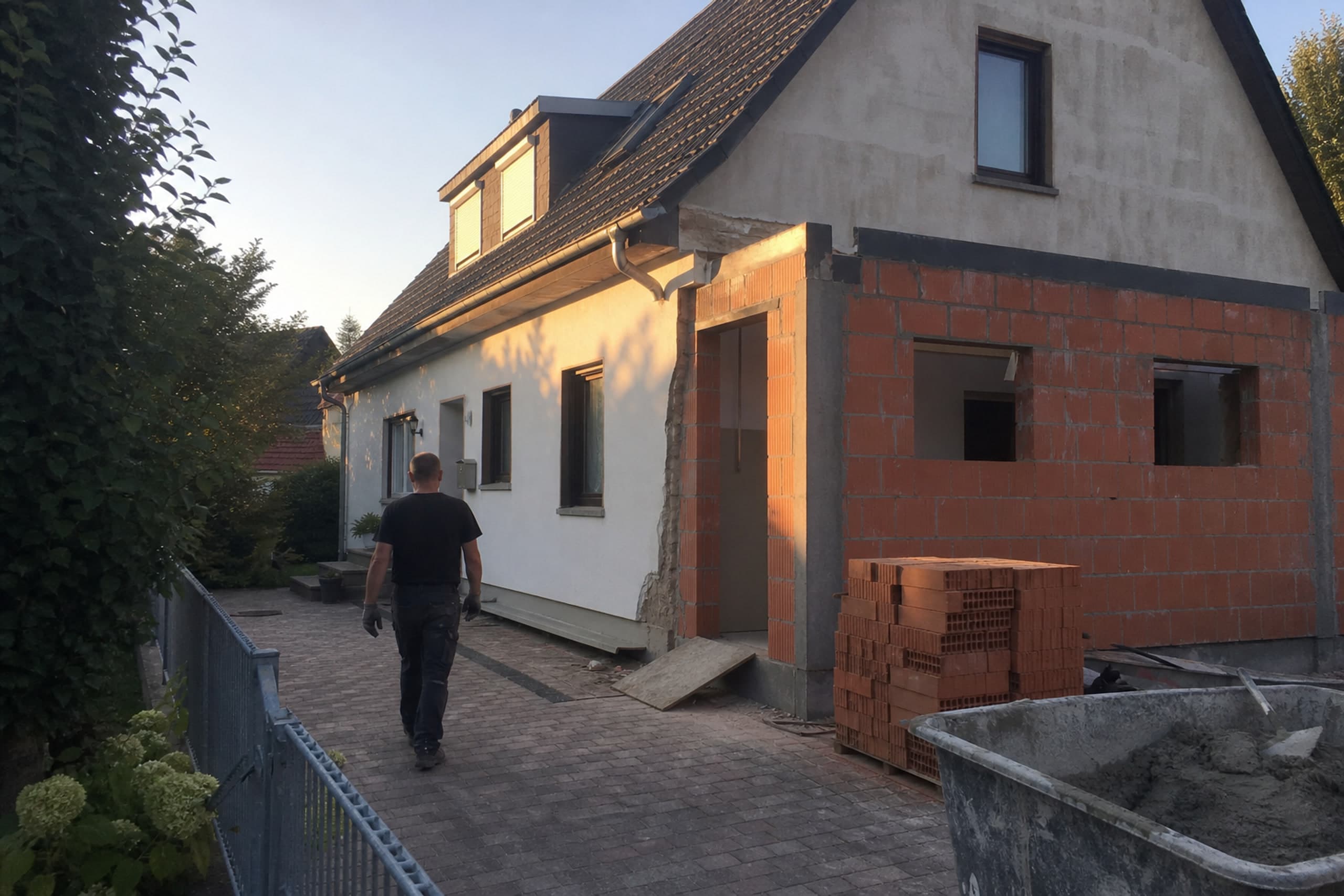 Anbau an einem Wohnhaus im Rohbau, Person geht mit dem Rücken zur Kamera zur Baustelle